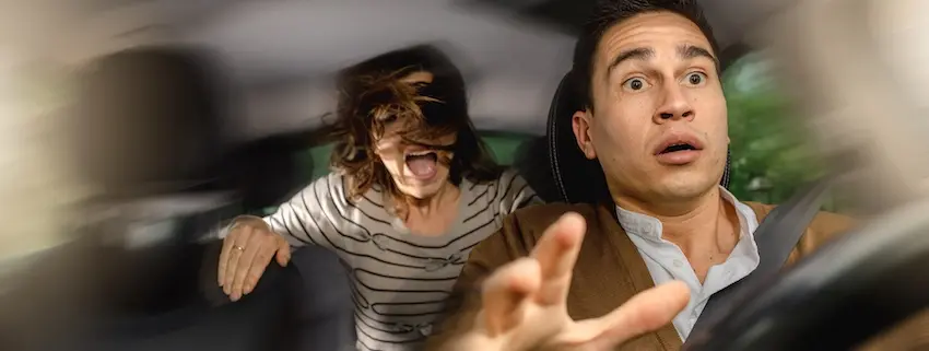 A wide-angle interior shot captures the terrifying split second of a car accident from inside the vehicle cabin showing a male driver in a tan jacket and white shirt in the right foreground with his eyes wide open in shock and his arm extended outward in a bracing gesture while a female passenger in a black and white striped shirt on the left is thrown violently forward with her hair whipping across her face and her mouth open in a scream- the entire image blurred with motion to convey the sudden and chaotic force of the impact in Illinois.