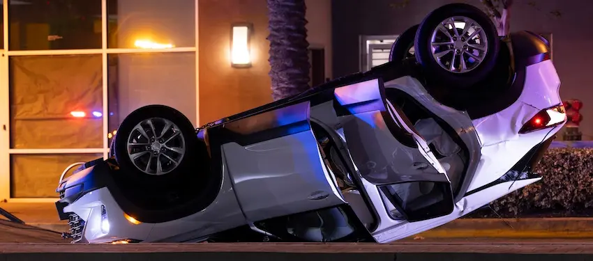 A white vehicle lies completely overturned on its roof at night with police lights visible in the background- depicting the kind of severe rollover crash that results in serious injuries and forms the basis of a high-stakes car accident case pursued by an experienced attorney from Illinois Lawyers 365.