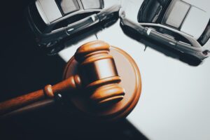 A wooden judge's gavel rests on its sound block in front of two toy cars positioned in a collision against a dark background- symbolizing the legal proceedings that follow when an injured victim brings a car accident case before the court to seek damages in Illinois.