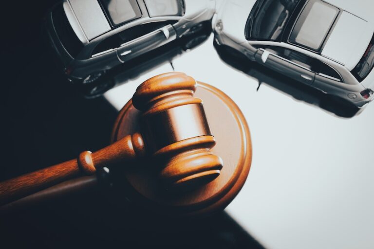 A wooden judge's gavel rests on its sound block in front of two toy cars positioned in a collision against a dark background- symbolizing the legal proceedings that follow when an injured victim brings a car accident case before the court to seek damages in Illinois.